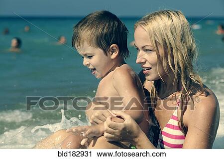 Wave splashing on mother holding son on beach View Large Photo Image Stock Image - Wave splashing on mother holding son on beach. Fotosearch