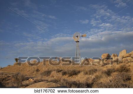Stock Image - Windmill over rock formations in desert field. Fotosearch