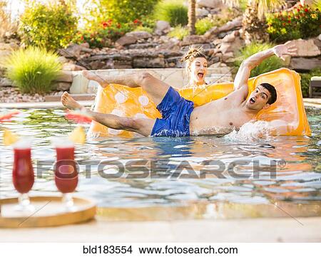 Picture - Woman pushing boyfriend in swimming pool. Fotosearch