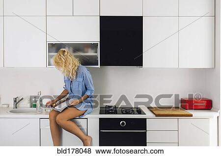 Stock Photo - Woman reading on kitchen counter. Fotosearch