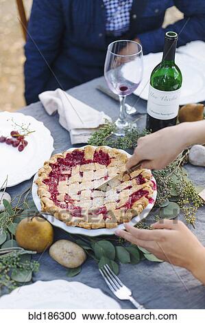 Stock Image - Woman serving pie at outdoor table. Fotosearch