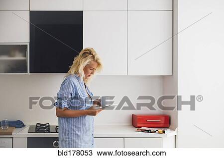 Stock Image - Woman using digital tablet in kitchen. Fotosearch