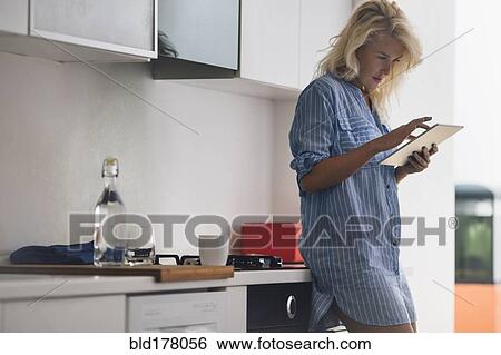 Stock Photograph - Woman using digital tablet in kitchen. Fotosearch