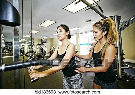 Stock Image - Woman working out with trainer in gymnasium. Fotosearch
