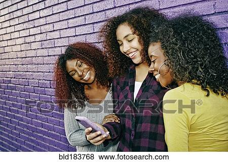 Stock Photo - Women using cell phone outdoors at purple wall. Fotosearch