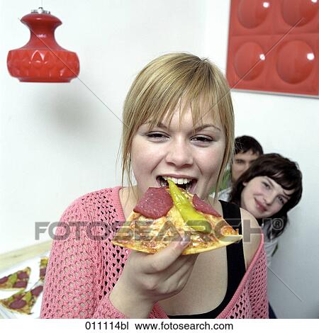 Stock Image - Blonde teenager biting in slice of pizza. Fotosearch