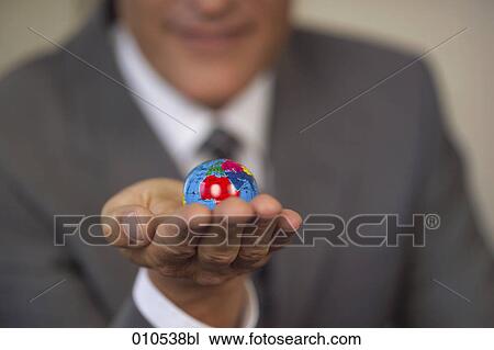 Stock Image - businessman holding a miniature globe in the palm of his hand. Fotosearch