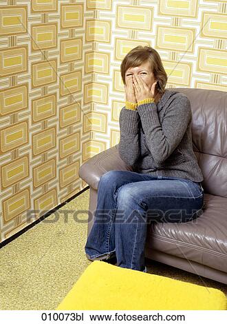 Stock Image - caucasian woman sitting on grey sofa laughing. Fotosearch