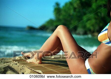 Stock Image - close-up of young woman in bikini sitting on a tropical beach. Fotosearch