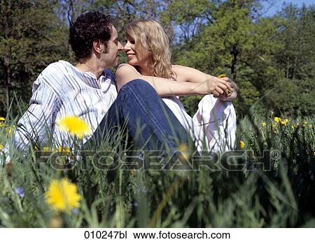Stock Image - couple in love (35-40 years) sitting in the grass flirting. Fotosearch