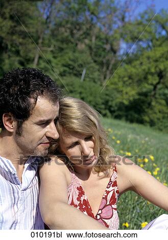 Stock Image - couple in love sitting in the grass close to each other. Fotosearch