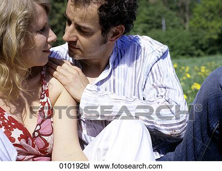 Stock Image - couple in love sitting in the grass close to each other. Fotosearch