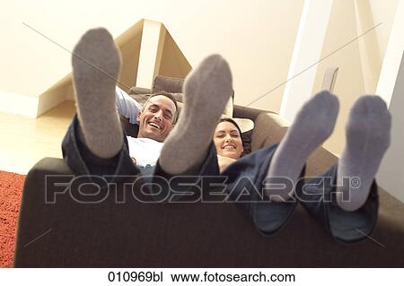 Stock Image - Couple lying on couch with their feet up. Fotosearch
