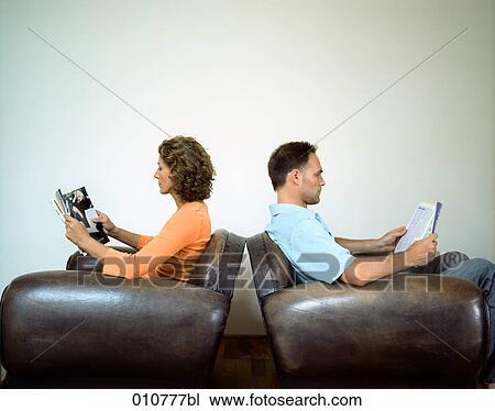 Stock Image - couple sitting back to back in arm chairs reading magazines. Fotosearch