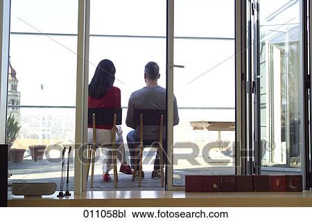 Stock Image - Couple sitting on a terrace seen from their living room. Fotosearch
