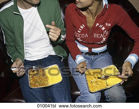 couple sitting on sofa eating take-away food from alluminium tray on their laps View Large Photo Image Stock Image - couple sitting on sofa eating take-away food from alluminium tray on their laps. Fotosearch