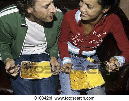 couple sitting on sofa eating take-away food from alluminium tray on their laps View Large Photo Image Stock Image - couple sitting on sofa eating take-away food from alluminium tray on their laps. Fotosearch