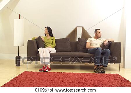 Stock Image - Couple sitting on sofa looking in different directions. Fotosearch