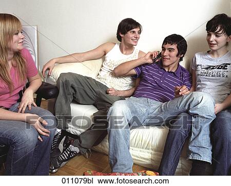 Four teenagers sitting together one using a mobile phone View Large Photo Image Stock Image - Four teenagers sitting together one using a mobile phone. Fotosearch