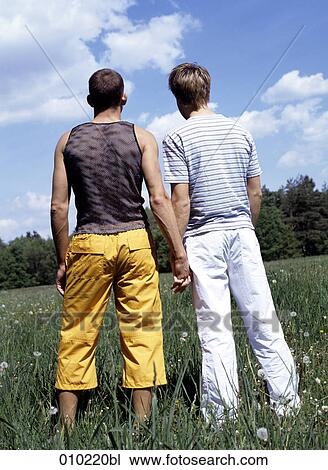 Stock Image - gay couple (20-25 years) holding hands, view from behind. Fotosearch