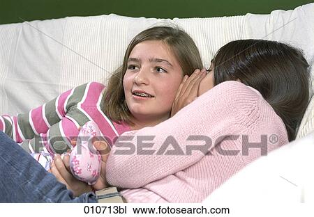 Stock Image - girl sitting on sofa whispering in another girl´s ear. Fotosearch