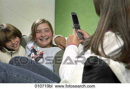 Stock Image - girl taking picture with mobile phone of little boy embracing his friend. Fotosearch