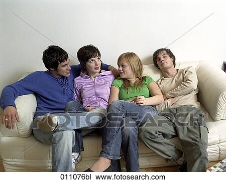 Stock Image - Group of friends sitting on sofa and talking to each other. Fotosearch