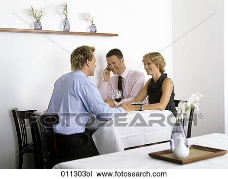 Stock Image - group of three business people in a restaurant, one talking on a mobile. Fotosearch
