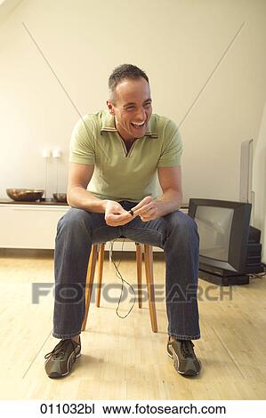 Laughing young man sitting in his living room View Large Photo Image Stock Image - Laughing young man sitting in his living room . Fotosearch