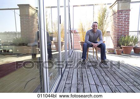 Laughing young man sitting on terrace of his home View Large Photo Image Stock Image - Laughing young man sitting on terrace of his home. Fotosearch