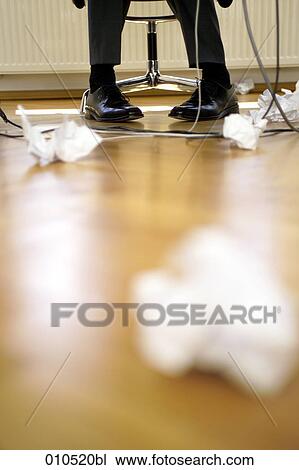 Stock Image - legs of businessman under the table with crumpled paper lying on the floor. Fotosearch