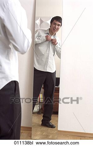 Stock Image - Male teenager laughing while buttoning his shirt. Fotosearch