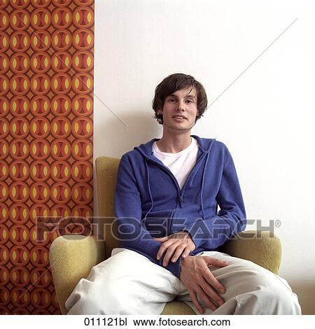 Stock Image - Male teenager sitting in front of colourful wallpaper. Fotosearch