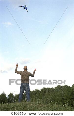 Stock Image - man flying a blue kite near the woodside. Fotosearch