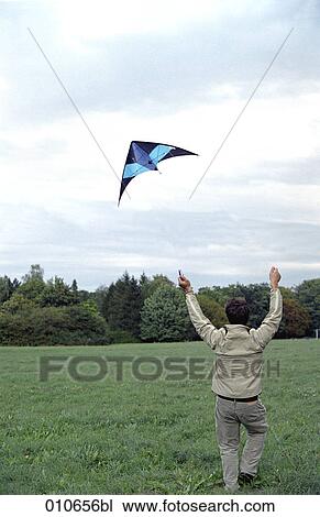 Stock Image - man in a meadow flying a blue kite . Fotosearch