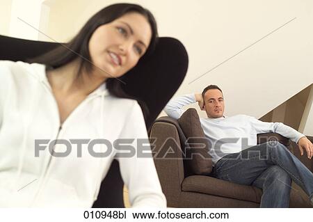 Stock Image - Man looking suspiciously at his girlfriend sitting in the foreground. Fotosearch