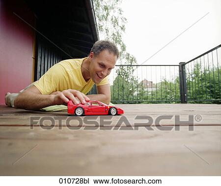 man lying on balcony playing with red toy car View Large Photo Image Stock Image - man lying on balcony playing with red toy car. Fotosearch