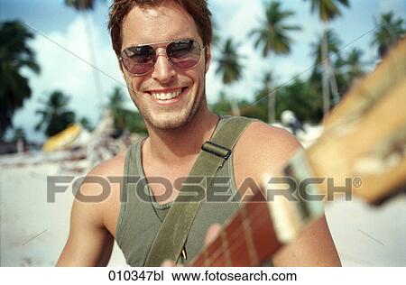 Stock Image - man on the beach playing his guitar. Fotosearch