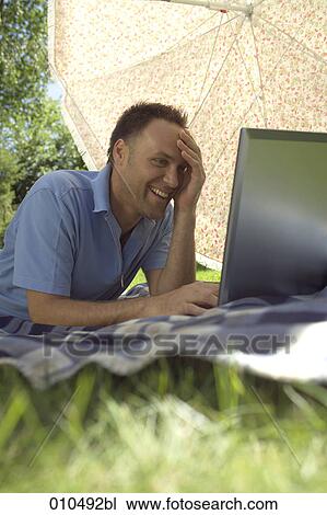 Stock Image - man reading something pleasant on his laptop. Fotosearch