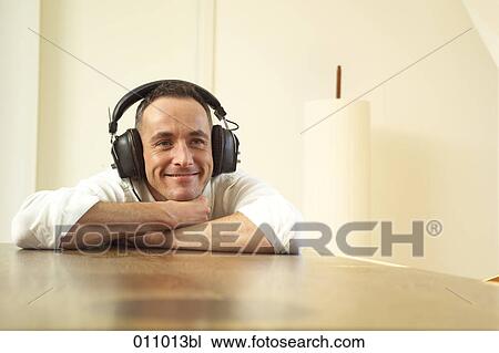 Stock Image - Man resting his head on a table an listening to music. Fotosearch