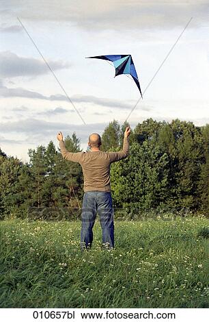 Stock Image - man standing in a meadow and flying a blue kite. Fotosearch