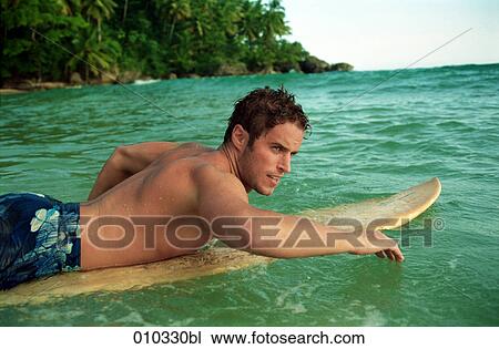 Stock Image - man swimming in the water lying on his surfboard. Fotosearch