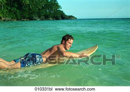 Stock Image - man swimming in the water lying on his surfboard. Fotosearch