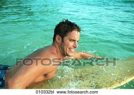 Stock Image - man swimming in the water lying on his surfboard. Fotosearch