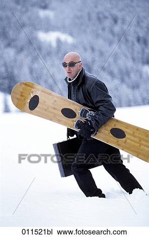 Stock Image - man walking in snow with snowboard and briefcase. Fotosearch