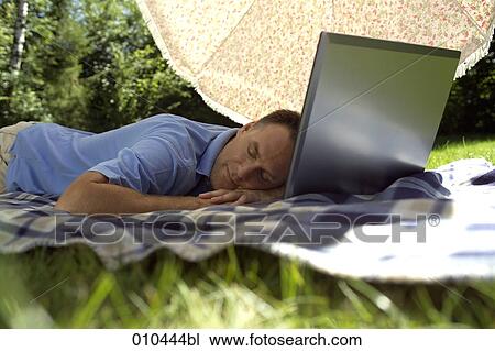 Stock Image - man with his laptop computer under a sunshade, day-dreaming. Fotosearch