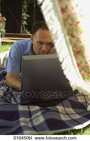 Stock Image - man working with laptop in his garden. Fotosearch
