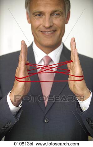 Stock Image - mature businessman doing the cat´s cradle with a red woolen thread. Fotosearch