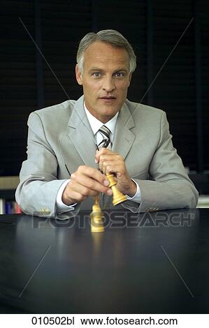 mature businessman sitting at desk and playing with chess pieces View Large Photo Image Stock Image - mature businessman sitting at desk and playing with chess pieces. Fotosearch