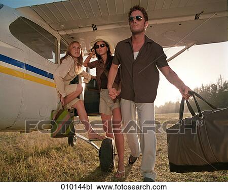 Stock Image - one man and two women posing like fashion models near small propeller plane. Fotosearch